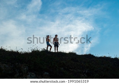 A low angle shot of two shirtless Mexican guys standing on a hill under a bright blue cloudy sky