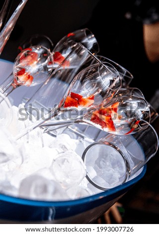 A vertical shot of wine glasses with sliced strawberries in a bucket with ice cubes in a bar