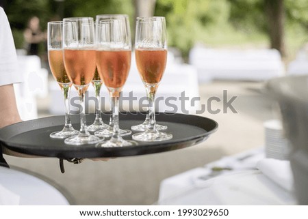 A closeup shot of the waiter\'s hand holding a tray of champagne glasses outside