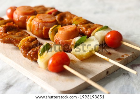 A shallow focus shot of juicy skewers with meat   vegetables on a wooden board and a marble tabletop