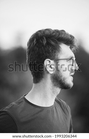 A vertical grayscale shot of a handsome Bosnian man with glasses from the side, looking ahead with bright light shining on his face