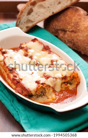 A vertical shot of cannelloni stuffed with goat cheese and arugula with cheese and tomato sauce