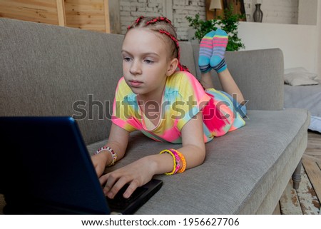 Girl engaged on laptop while lying the sofa in room at home. Concept education is process teaching at school. Teenager studying the computer. Copy space