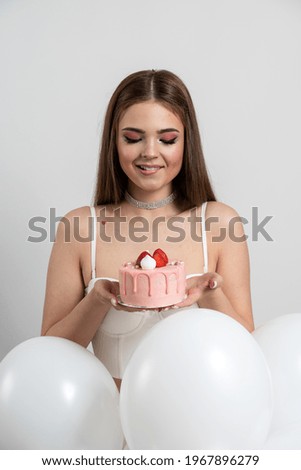 Attractive, well-groomed girl holds an appetizing cake, looks at it sincerely, wants to eat it. Beautiful, young woman on a white background
