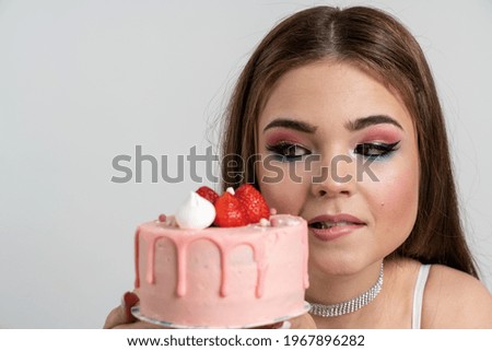 Close up view. A young, charming girl looks at the cake, she really wants to eat it. Cute girl with a cake on a white background