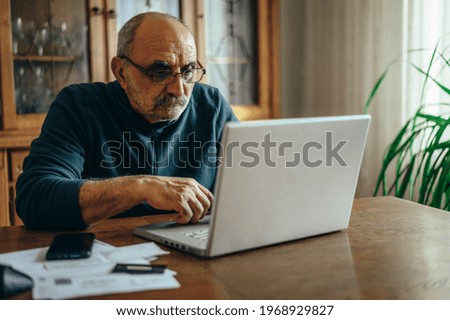 Senior man using a laptop while relaxing at home and surfing the internet