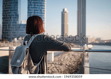 Happy young female traveler in the big city of Dubai, Blue Water Island. Luxury and comfortable tourism season in United Arab Emirates. Back or rear view of young woman in dress and backpack