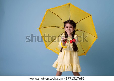 Happy cute little Girl Indian in red rubber boots, cotton dress holds in her hands yellow umbrella on a blue background in the studio. concept Spring, space for text