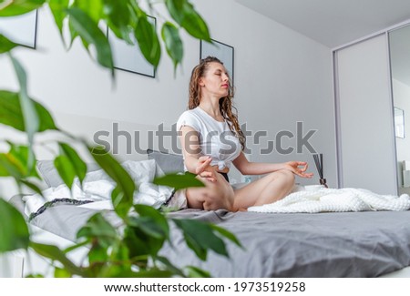Young business woman meditates while sitting on the bed, after work. Girl listens calm music near telephone. Comfort zone and wellness concept. Yoga at home