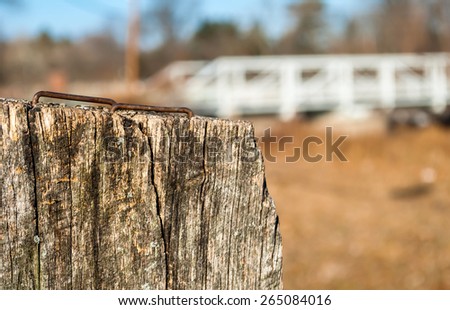 Fence post in remote area with iron bridge background, Wooden stump with rusty nails on top, fall weather, bark, artistic and abstract view. Depth of field on steel bridge
