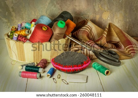 Sewing supplies: thread spools in a basket, fabric, needles, chalk, scissors. Toned photo. Selective focus