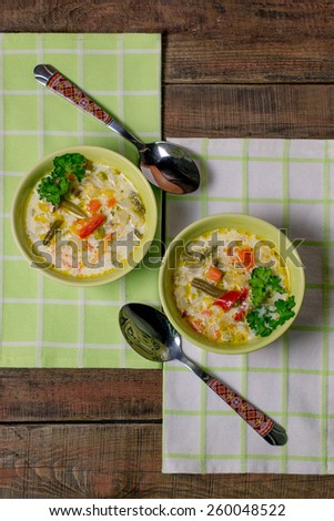 Two bowls of vegetable soup with cheese on a green napkin and wooden table