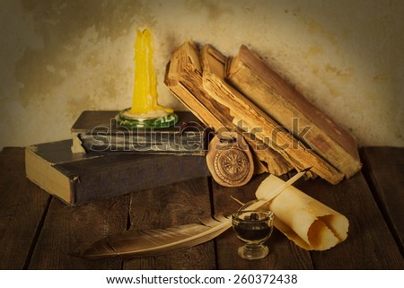 Old books, candle, amulet, pen, ink bottle, roll on the wooden background. Selective focus. Toned photo