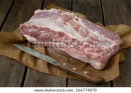 Piece of fresh meat and knife on wrapping paper and wooden background
