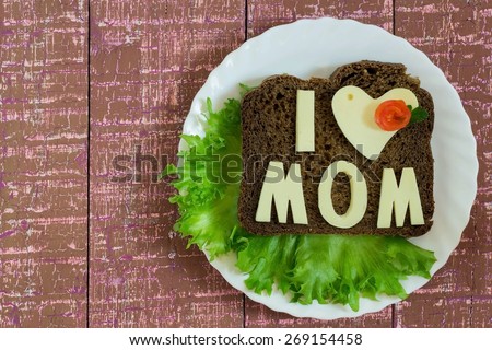 Big sandwich with brown bread, green salad and cheese letters I love mom