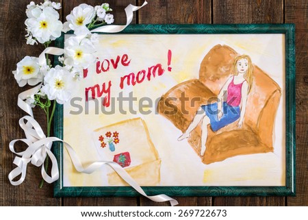 Drawing child for Mother\'s Day with the words I love my mom in a green frame, flowers and a ribbon on the wooden background
