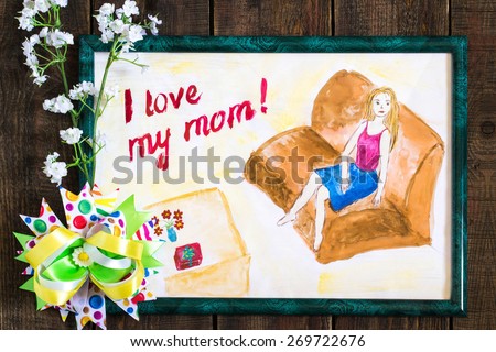 Drawing child for Mother\'s Day with the words I love my mom in a green frame, flowers and bow on a wooden background