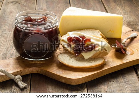 Onion jam, white bread with cheese, a jar of jam, a piece of cheese on the board and a wooden table. Selective focus.