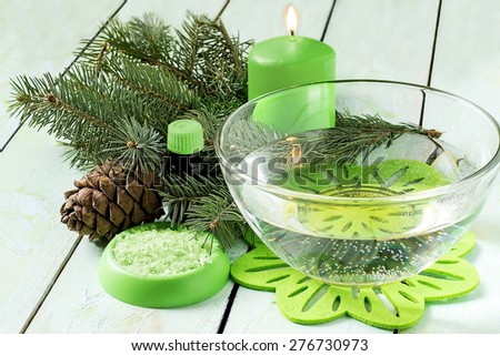 Coniferous SPA concept: bath with sea salt and cedar oil, pine branch with cones, sea salt, oil in the bottle and scented candle on a light green painted wooden background. Selective focus