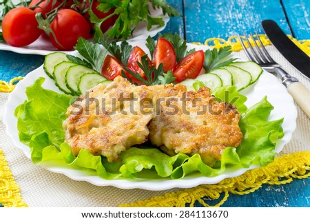 Delicious homemade pork cutlets with vegetables on a plate, napkin with yellow trim and cutlery on a blue wooden background. Selective focus