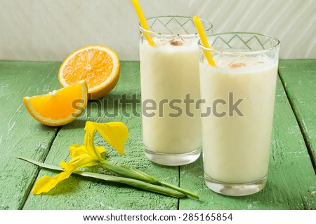 Fresh homemade milkshake with ice cream, orange juice and nutmeg in a glass with cocktail straws, slices of orange, iris flower on a green wooden table. Selective focus