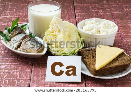 Products containing calcium (sardines in oil, cabbage, milk, cottage cheese, brown bread, cheese) on wooden burgundy background