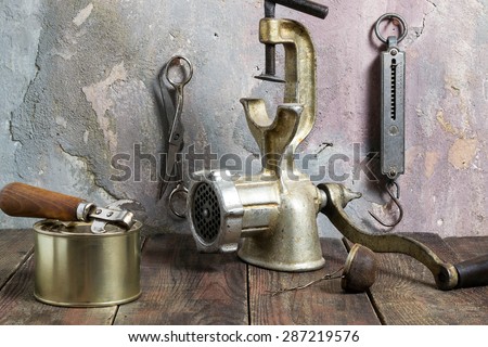 Outdated items Kitchen steelyard, scissors, manual grinder, tea strainer, can, can opener on a wooden table against a wall with an old plaster. Photo of vintage style