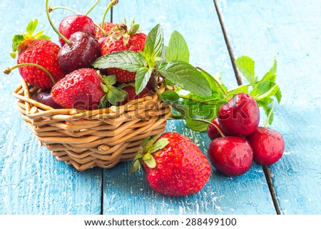 Freshly ripe strawberries and cherries with water drops and mint in a basket on a blue wooden table