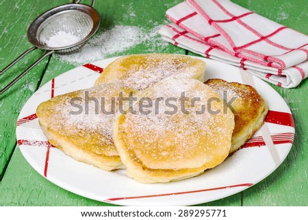 Fritter with powdered sugar - a traditional russian breakfast on a plate, sieve with powdered sugar, a napkin in a cage on a green wooden table. Selective focus