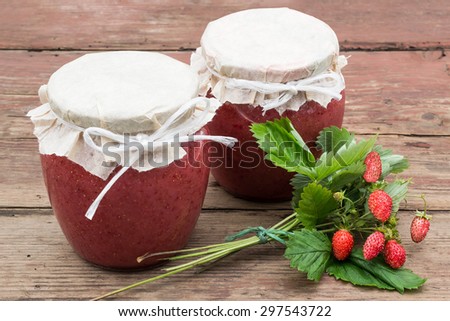 Fresh puree of wild strawberries with sugar - vitamin canned in jars and bouquet with berries on the old rustic table. Selective focus