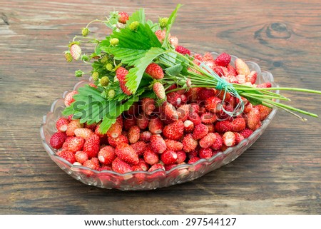 Dish filled with fresh sweet berries of wild strawberries, a bouquet of strawberries on top