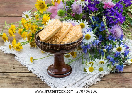 Bouquet of bright wildflowers and cookies in a vintage ceramic vase on an old rustic table. Selective focus