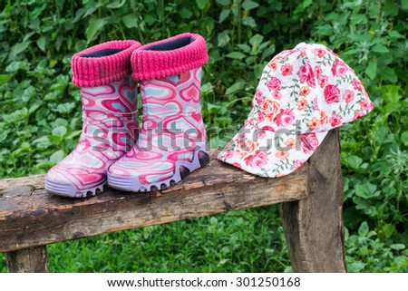 Children rubber boots and a cap to work in the garden on the old dilapidated bench