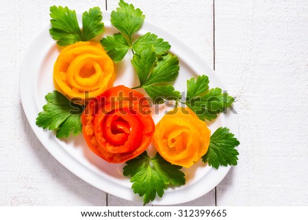 Home decoration for festive dishes - roses of yellow and red tomatoes with leaves of parsley, a plate on white wooden background with copy space