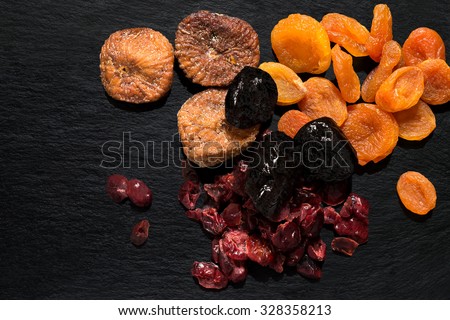 Various dried fruits: apricots, figs, prunes, cranberries on a slate plate