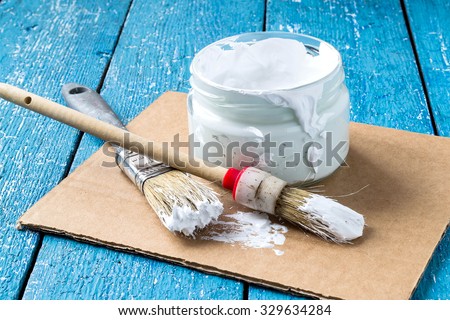 White viscous paint to repair the premises in a glass jar, brush on cardboard and blue wooden table. Selective focus