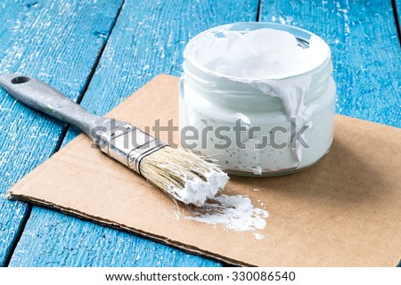 White viscous paint to repair the premises in a glass jar, brush on cardboard and blue wooden table. Selective focus