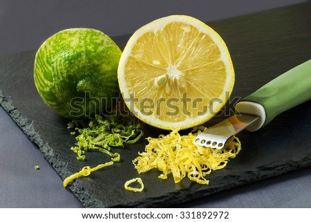Juicy lime and lemon, citrus zest and knife to peel on a slate plate