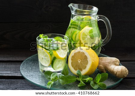 Fresh cold water with lemon, cucumber, ginger, mint and ice in a pitcher and glass on a glass tray