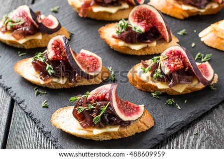 Canape or crostini with toasted baguette, cheese, onion jam, figs and fresh thyme on a slate board. Delicious appetizer, ideal as an aperitif. Selective focus