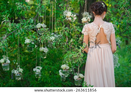Young beautiful bride standing with his back amid banks decorated with roses tree,decor,concept,wedding decorations