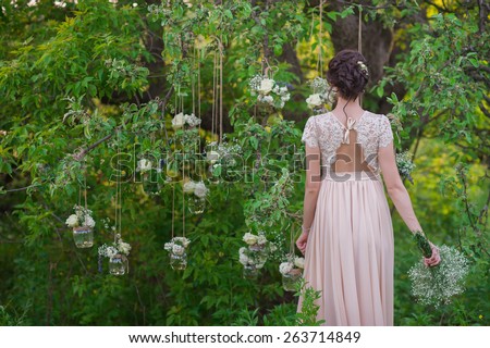 Young beautiful bride standing with his back amid banks decorated with roses tree,decor,concept,wedding decorations