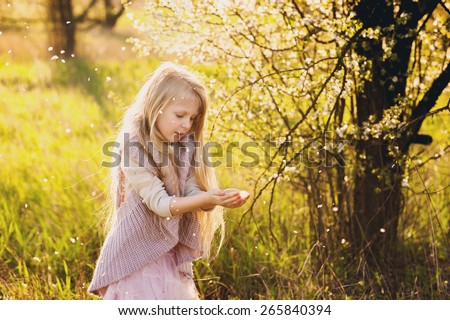 Little blond girl in the lush spring garden plays