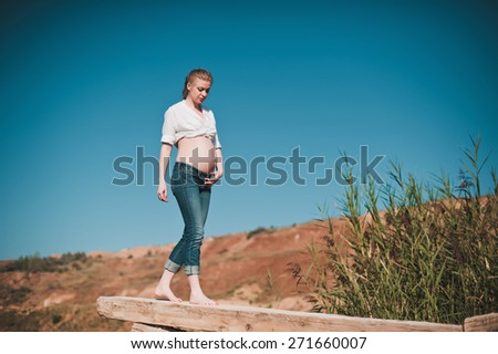 Beautiful young pregnant woman going on the pier on a blue lake, lifestyle, pregnancy, waiting