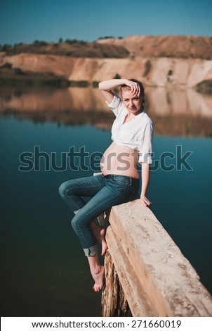 Beautiful young pregnant woman sitting on the pier on a blue lake, lifestyle, pregnancy, waiting