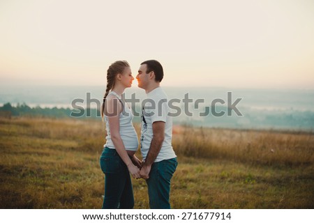 Young pregnant couple holding hands and standing in a field at sunrise