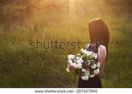 A young girl with a large bouquet of white flowers in a field at sunset, lifestyle