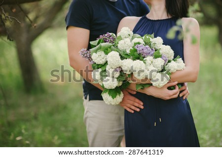 Young couple with a big bouquet of flowers is goes, embracing in nature, green grass, sunset, love, lifestyle