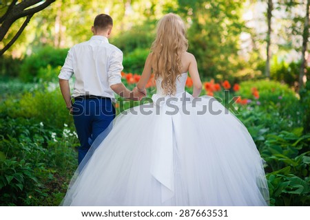 The bride and groom are in the park holding hands around the beautiful flower beds of poppies and white flowers