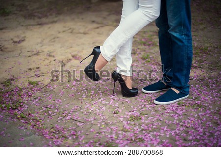 Beautiful legs of young girl in high heels next to the legs Man in pink flower petals, style, fashion, concept, romance